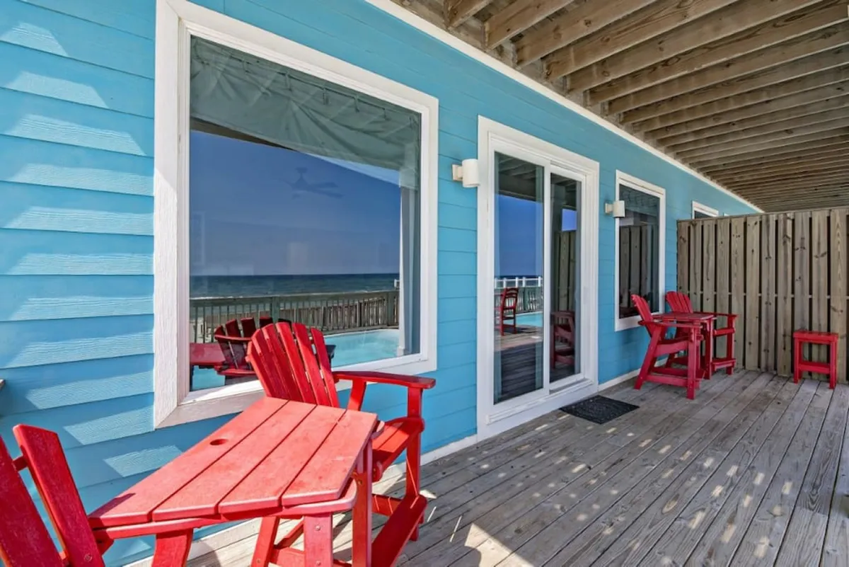 An inviting outdoor area featuring red Adirondack chairs, large windows, and a blue wall. The setup suggests a perfect spot for socializing or relaxing after a celebration, with the ambiance of beachfront leisure and comfort.