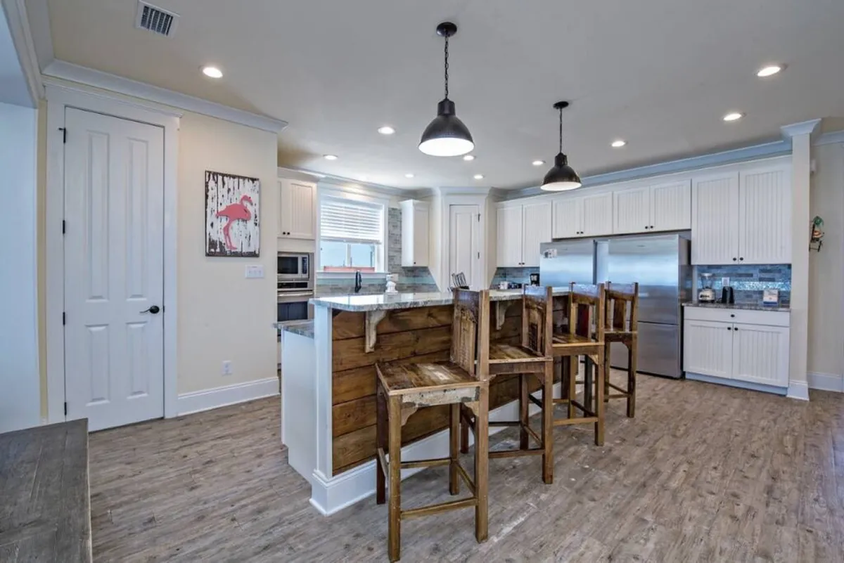 A modern, open kitchen featuring a large island with bar stools, white cabinetry, and high-end stainless steel appliances. The layout is spacious, encouraging multiple people to cook, socialize, or enjoy casual meals together. Natural light fills the room, making the space as inviting as it is functional.
