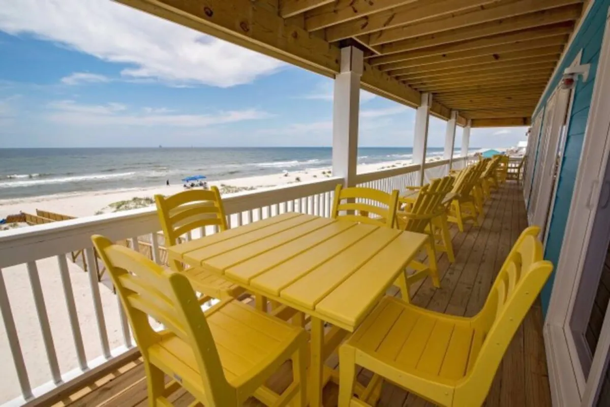 The photo focuses on a lively deck area with yellow chairs and a table overlooking the ocean. This outdoor space is ideal for shared meals, morning coffee, or evening gatherings, highlighting the property’s multiple decks and beautiful Gulf views for making memories and taking photos together.
