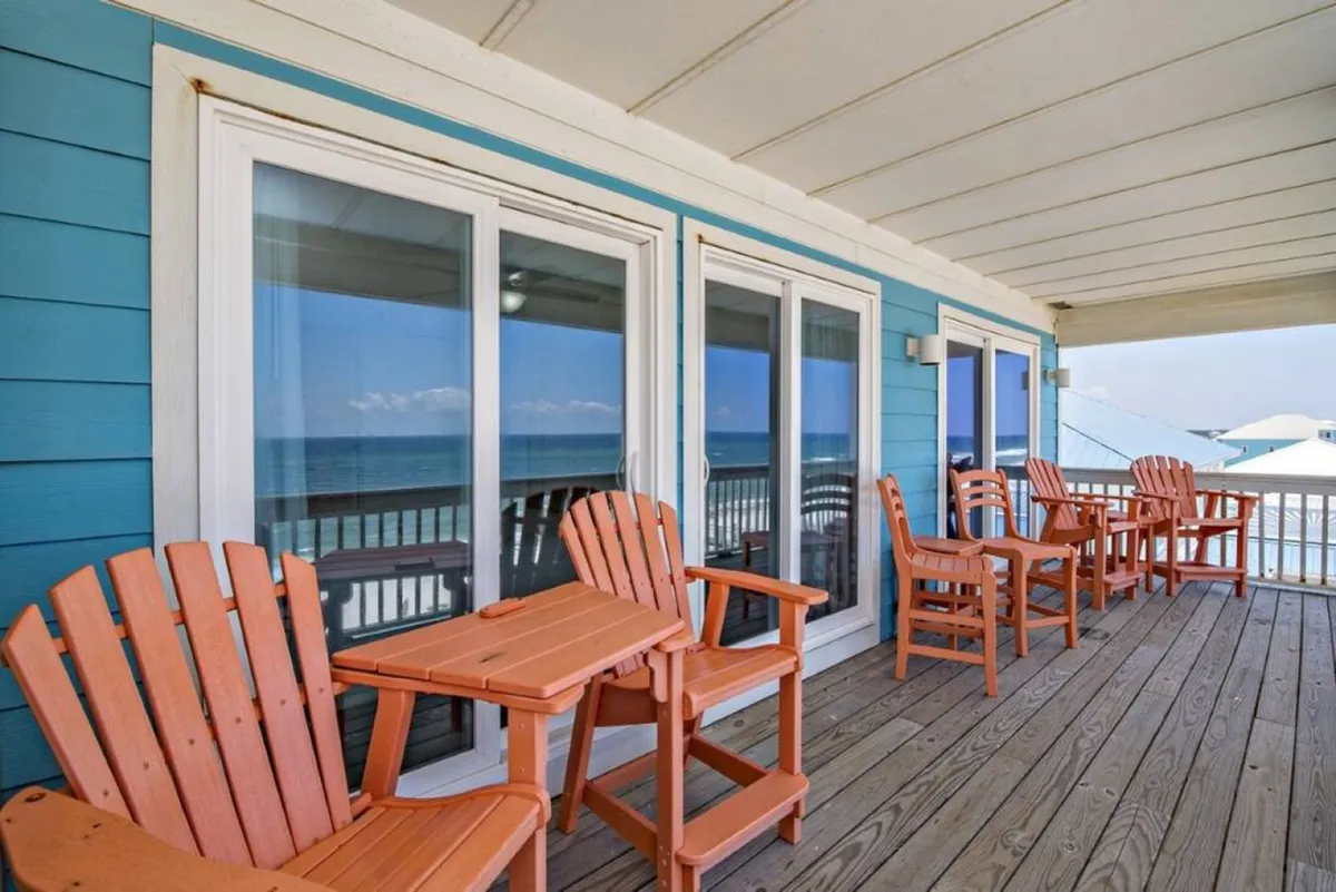 A tranquil deck scene with wooden chairs facing the ocean, framed by a classic railing. The view of the water beyond invites guests to envision group gatherings or quiet moments of inspiration overlooking the sea.