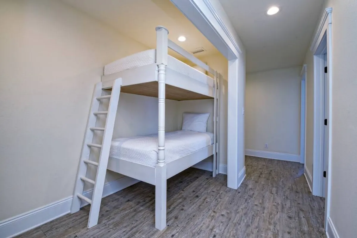 A playful yet cozy bunk room featuring a sturdy wooden bunk bed with a ladder, comfortable bedding, and soft lighting. The arrangement is clearly geared toward children or teens, creating a cheerful and safe sleepover space. The room is tidy and inviting, with enough space for sharing stories and making memories.