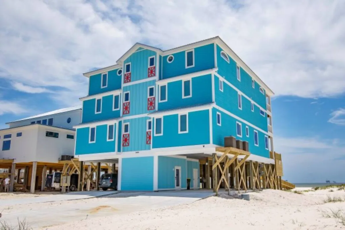 An exterior shot showing the estate’s bright blue facade with red accents and its elevated beachside structure. The vibrant colors and open design immediately establish a sense of place and privacy, underscoring the unique, inviting atmosphere of Easy Breezy.