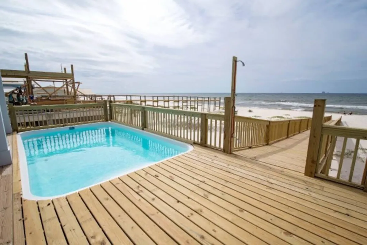An inviting exterior shot of a sparkling swimming pool on a deck with an open ocean view. Lounge chairs are positioned for relaxation, and the pool is an ideal spot for cooling off after a beach day.