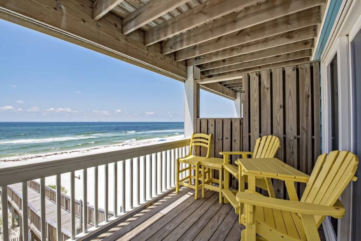 A tranquil balcony space featuring cheerful yellow chairs overlooking the ocean, with a wooden railing and open sky. The scene is bright and welcoming, perfect for enjoying morning coffee or evening drinks.
