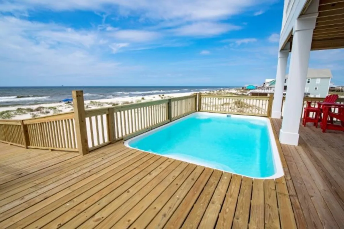 A stunning exterior deck overlooking a sparkling swimming pool and the ocean beyond. Ample lounge seating and a barbecue setup hint at effortless outdoor entertaining, while the pool and panoramic water views invite guests to relax or celebrate in style.